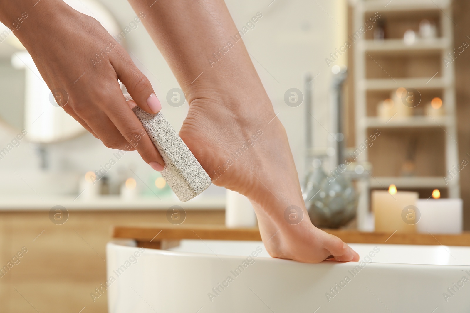 Photo of Woman using pumice stone for removing dead skin from feet in bathroom, closeup