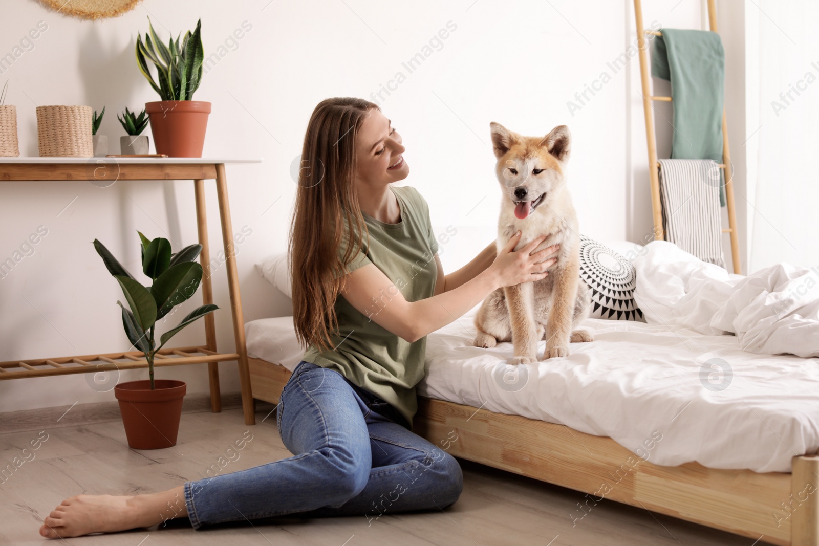 Photo of Young woman and Akita Inu dog in bedroom decorated with houseplants