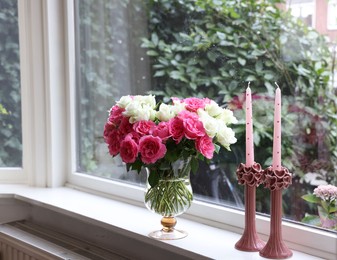 Photo of Vase with beautiful bouquet of roses and candles on windowsill indoors, space for text