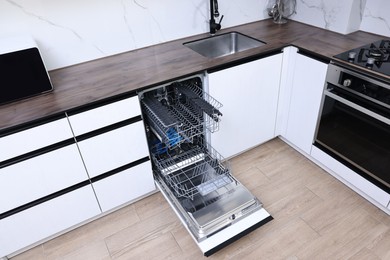 Photo of Open clean empty dishwasher in kitchen. Home appliance