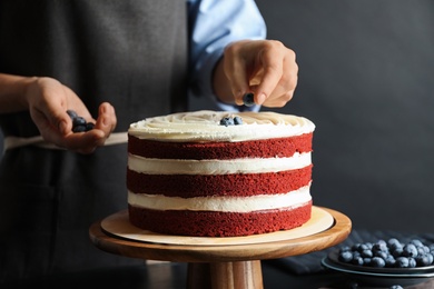 Woman decorating delicious homemade red velvet cake with blueberries at table