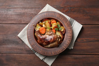 Photo of Tasty cooked rabbit meat with vegetables on wooden table, top view