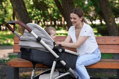 Happy nanny with cute little boy in stroller in park