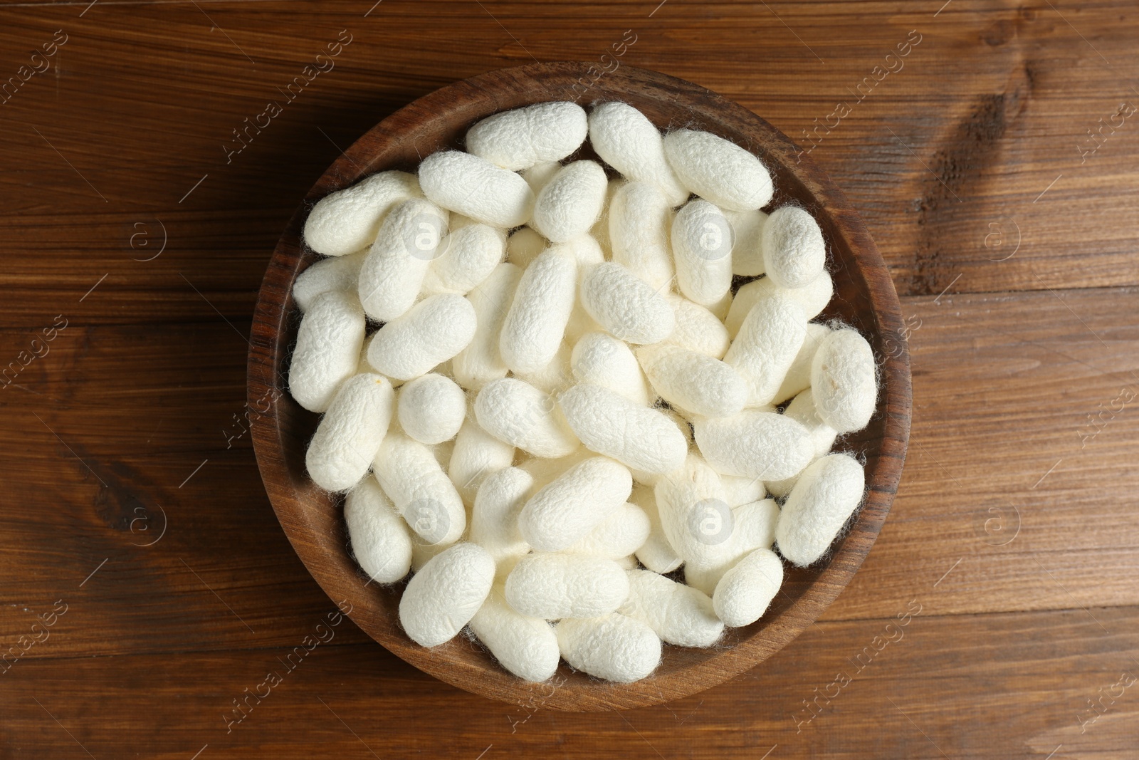 Photo of White silk cocoons in bowl on wooden table, top view