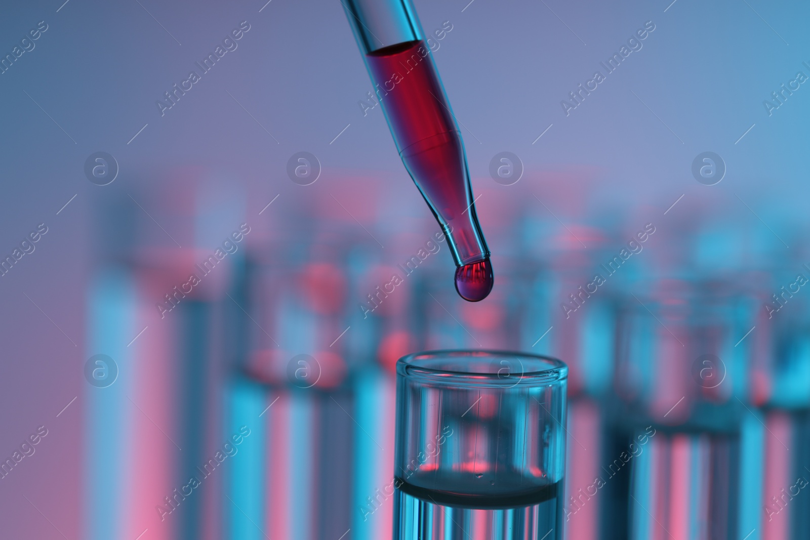 Photo of Dripping liquid from pipette into test tube on color background, closeup