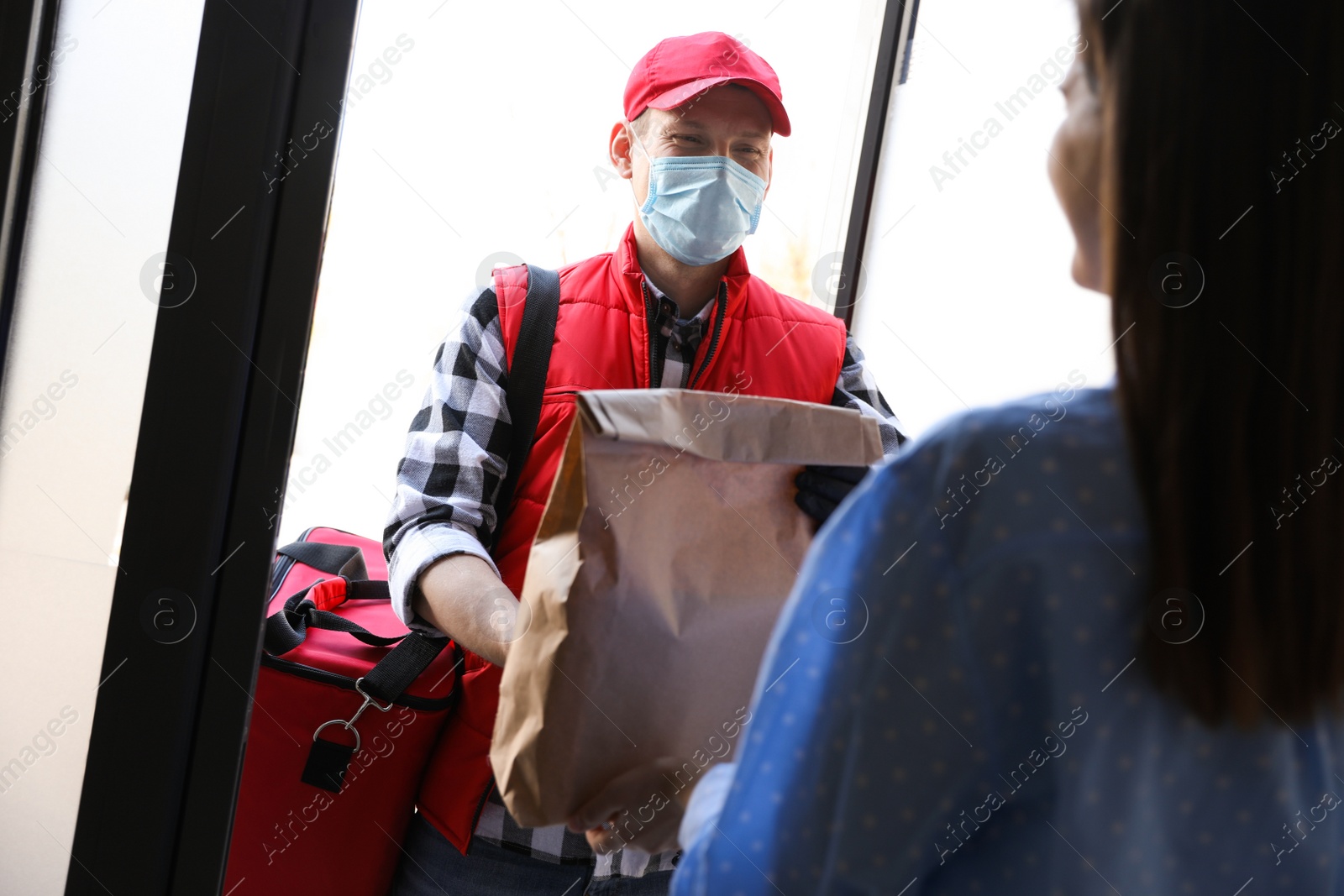 Photo of Courier giving order to woman at entrance. Delivery service during coronavirus quarantine