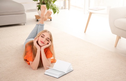 Photo of Young woman with book lying on floor at home