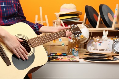 Photo of Woman playing guitar near table with many different stuff indoors, closeup. Garage sale