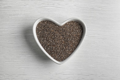 Photo of Heart shaped bowl with chia seeds on wooden background, top view