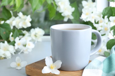 Photo of Cup of tea and fresh jasmine flowers on light grey table
