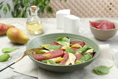 Photo of Delicious bresaola salad in bowl, fork and ingredients on light table