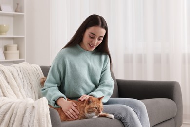 Photo of Beautiful woman petting cute cat on sofa at home