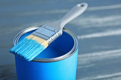 Paint can and dipped brush on wooden background, closeup