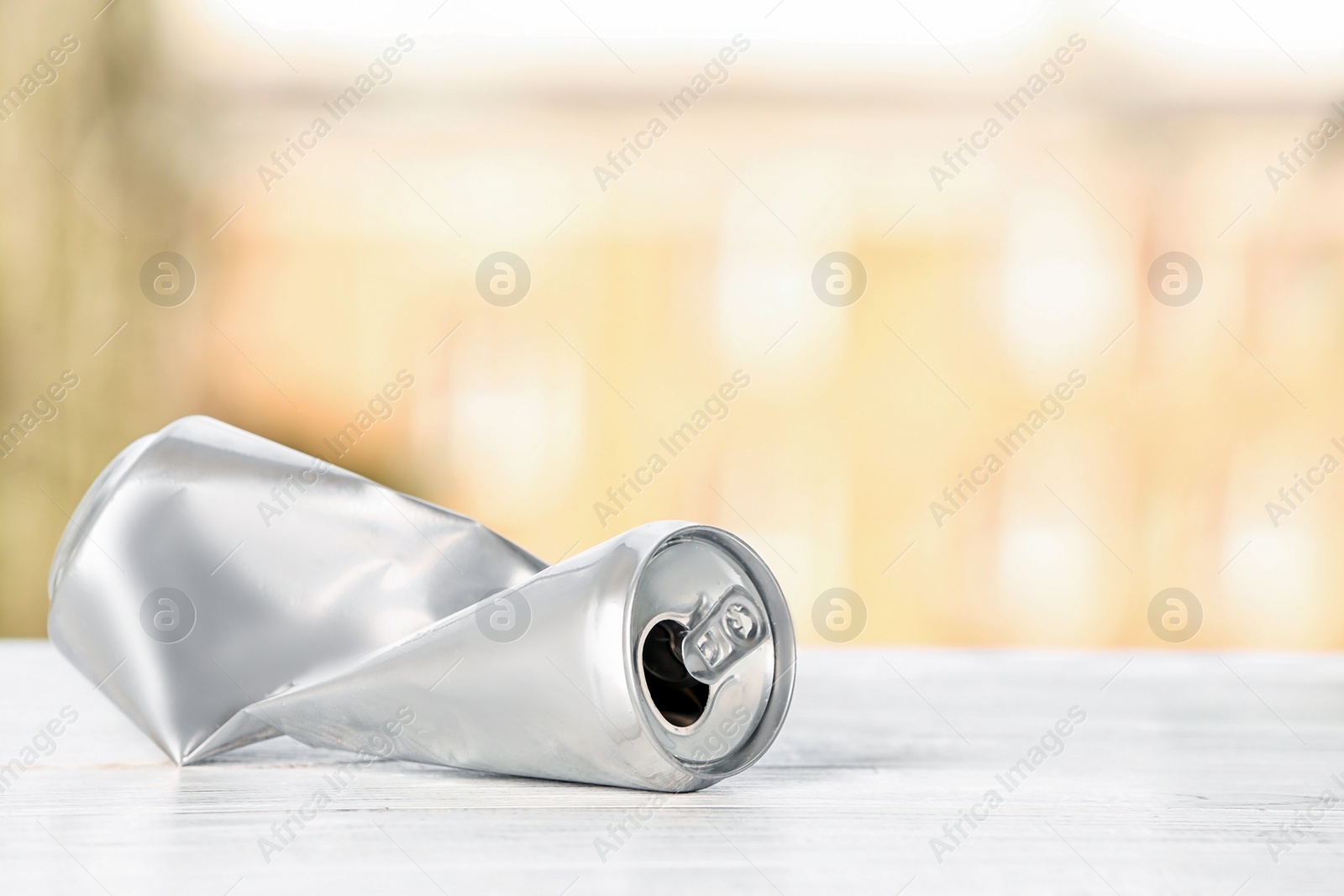 Photo of Crumpled aluminum can on table against blurred background. Metal waste recycling