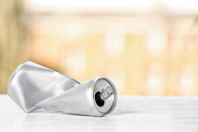 Crumpled aluminum can on table against blurred background. Metal waste recycling