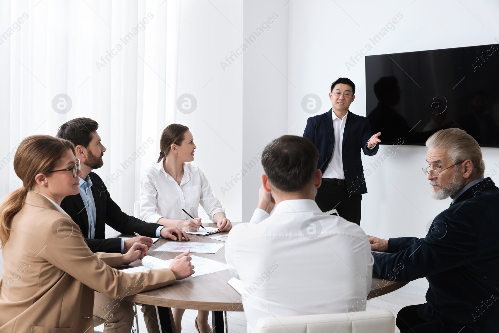 Photo of Business conference. Group of people listening to speaker report near tv screen in meeting room