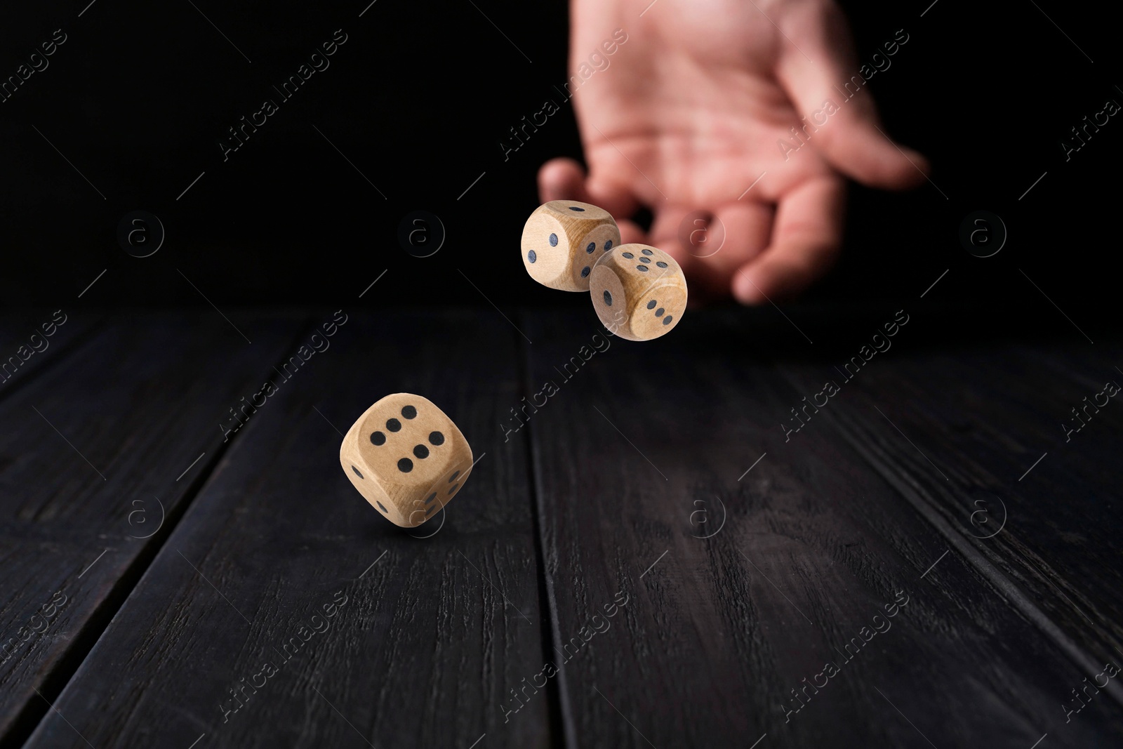 Image of Man throwing dice on black wooden table, closeup