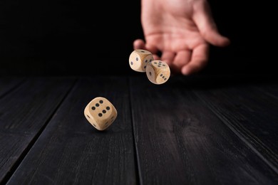 Man throwing dice on black wooden table, closeup