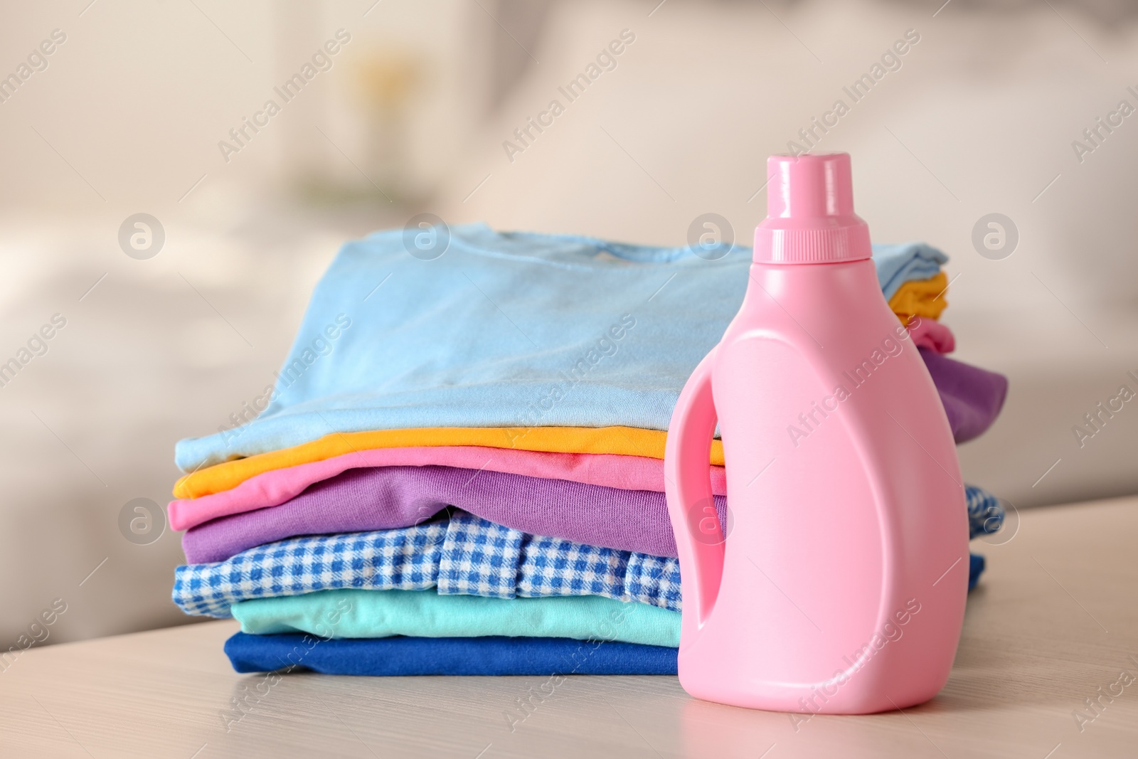 Photo of Stack of clean clothes and bottle with detergent on table