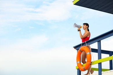 Photo of Female lifeguard with megaphone on watch tower against blue sky