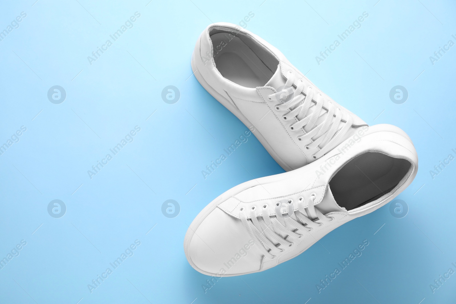 Photo of Pair of stylish white sneakers on light blue background, top view. Space for text