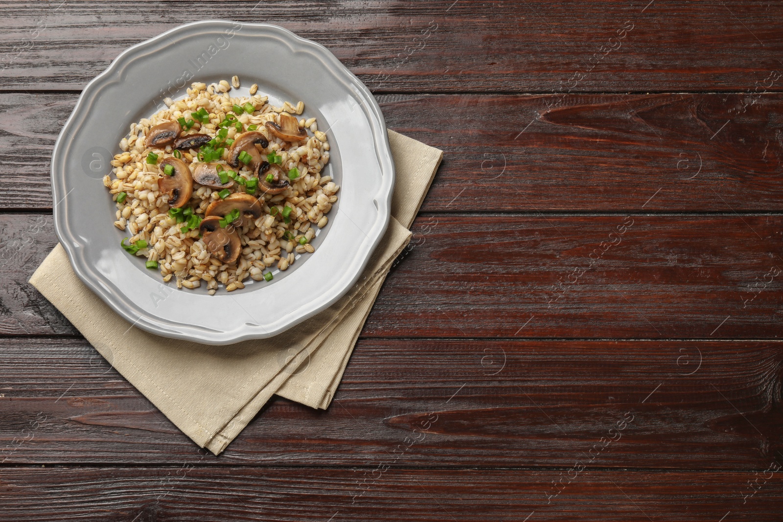 Photo of Delicious pearl barley with onion and mushrooms on wooden table, top view. Space for text