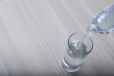 Pouring water from bottle into glass on wooden background. Space for text