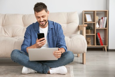 Happy man using smartphone while working with laptop at home