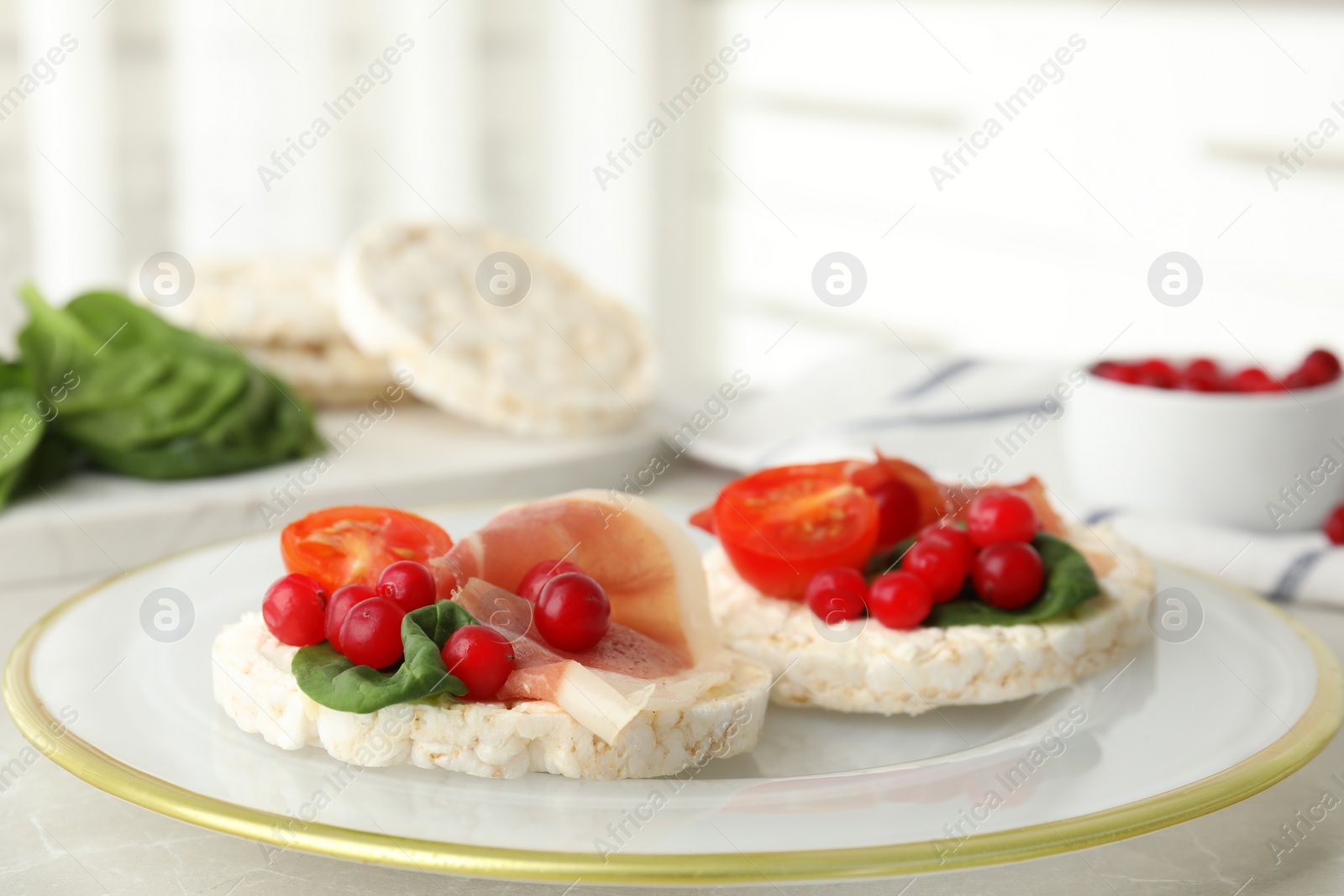 Photo of Puffed rice cakes with prosciutto, berries and basil on table, closeup