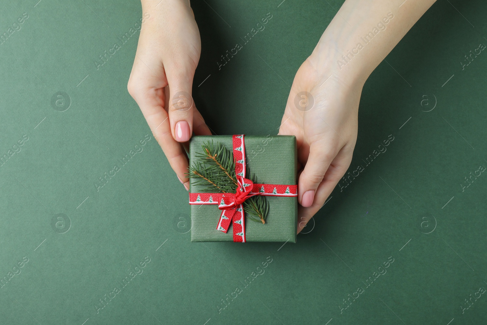 Photo of Woman holding beautifully wrapped Christmas gift box on dark green background, top view