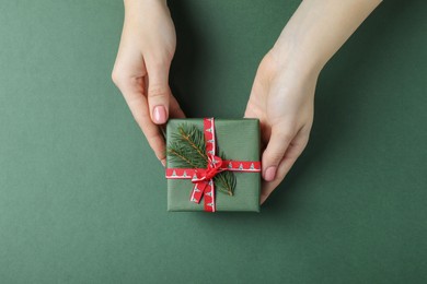 Woman holding beautifully wrapped Christmas gift box on dark green background, top view