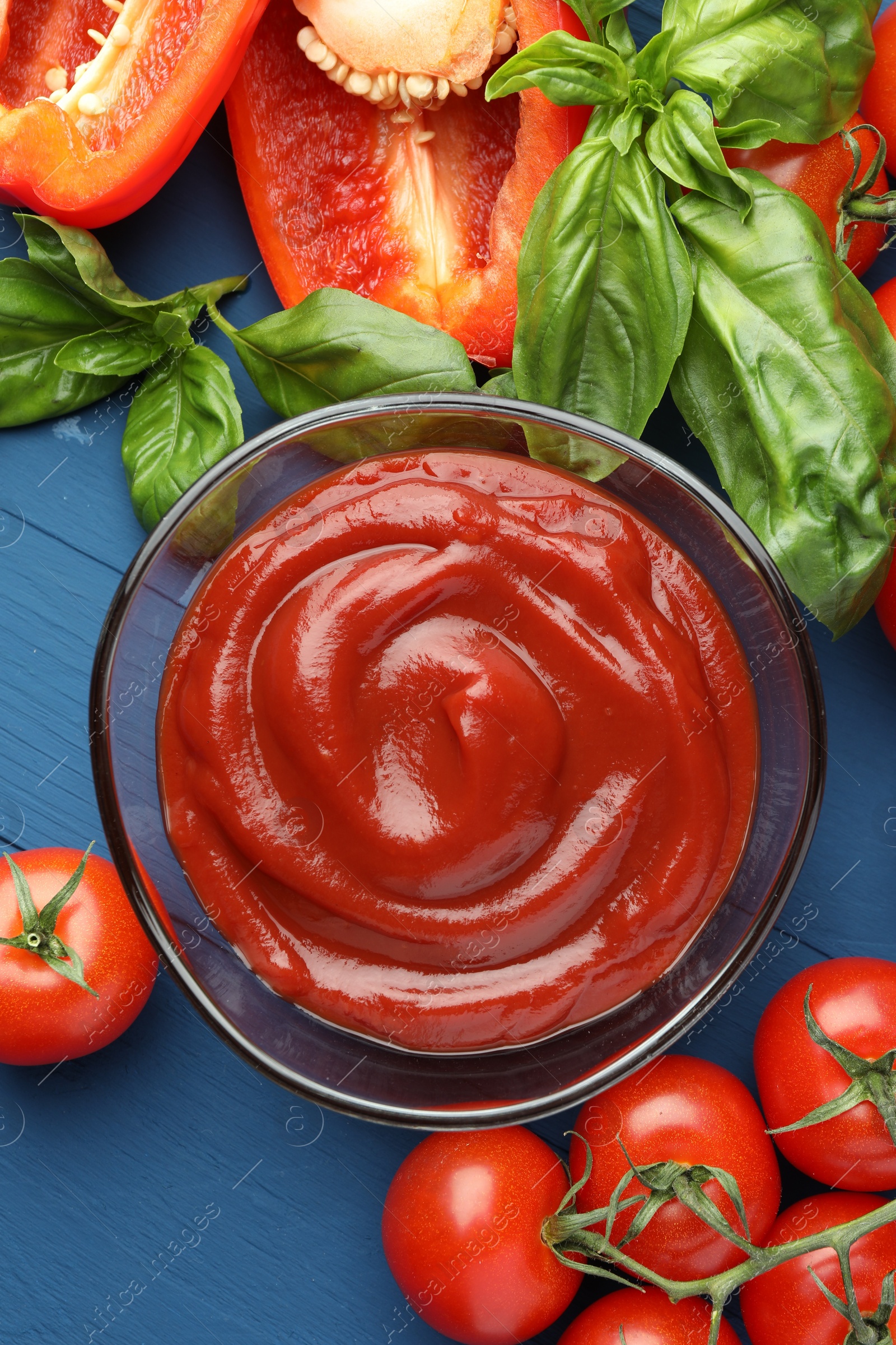 Photo of Bowl of tasty ketchup and ingredients on blue wooden table, flat lay