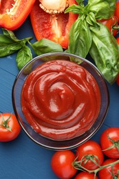 Photo of Bowl of tasty ketchup and ingredients on blue wooden table, flat lay