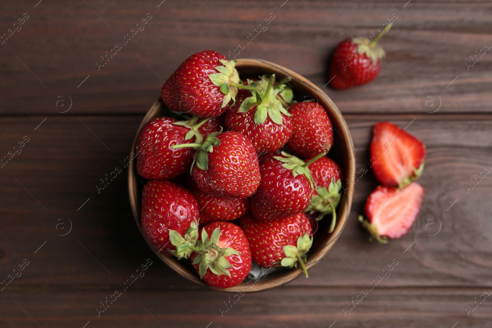 Photo of Delicious ripe strawberries in bowl on wooden table, flat lay