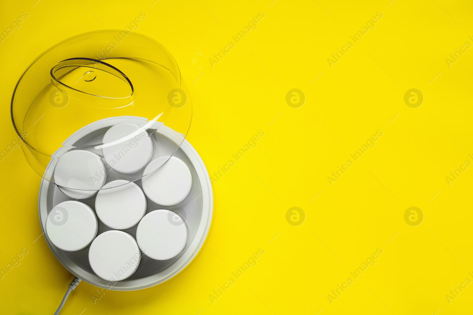 Photo of Modern yogurt maker with jars on yellow background, top view. Space for text