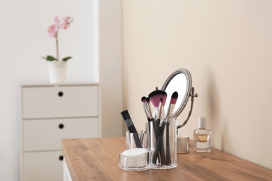 Photo of Organizer with cosmetic products for makeup and mirror on table against light wall