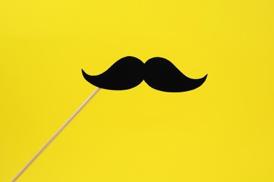 Photo of Fake paper mustache on stick against yellow background