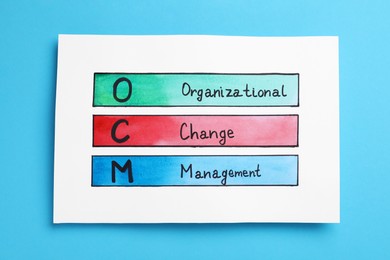 Photo of Paper with OCM abbreviation and its interpretation (Organizational Change Management) on light blue background, top view
