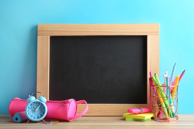 Different school stationery and small blank chalkboard on table near light blue wall. Space for text