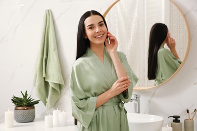 Beautiful young woman near mirror in bathroom