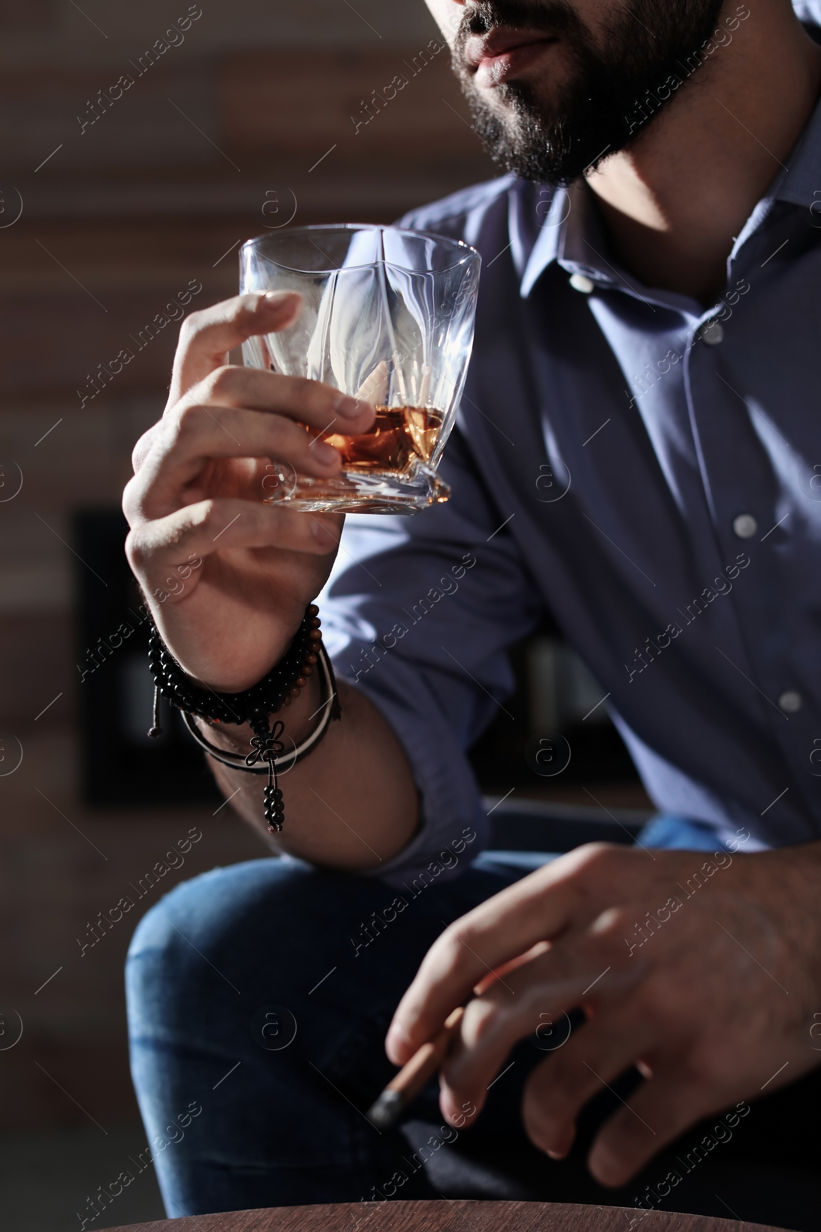 Photo of Man with glass of whiskey and cigar at home, closeup