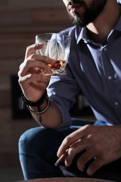 Man with glass of whiskey and cigar at home, closeup