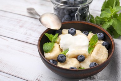 Photo of Bowl of tasty lazy dumplings with blueberries, sour cream and mint leaves on white wooden table. Space for text