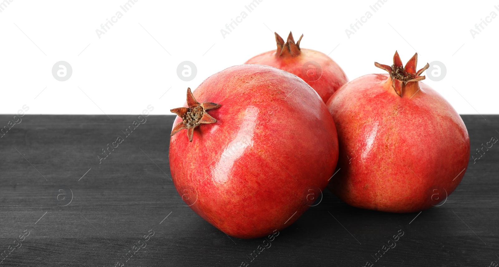 Photo of Fresh pomegranates on black wooden table against white background, space for text