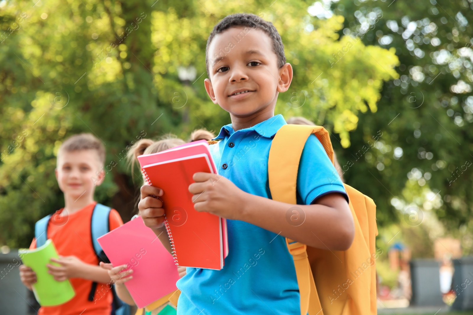 Photo of Cute little child with backpack and notebooks outdoors. Elementary school