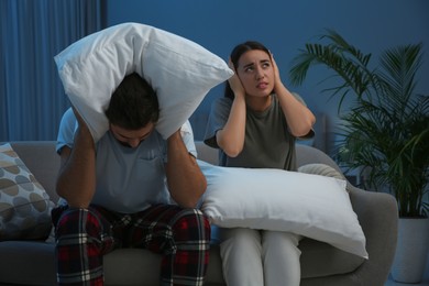 Photo of Young couple with pillows suffering from noisy neighbours in living room at night