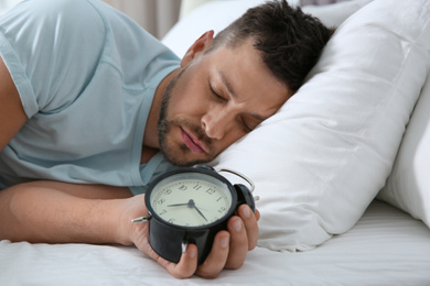 Man sleeping with alarm clock at home in morning