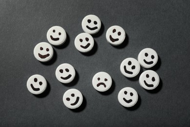 Photo of Pill with sad face among happy ones on black background, flat lay. Depression concept