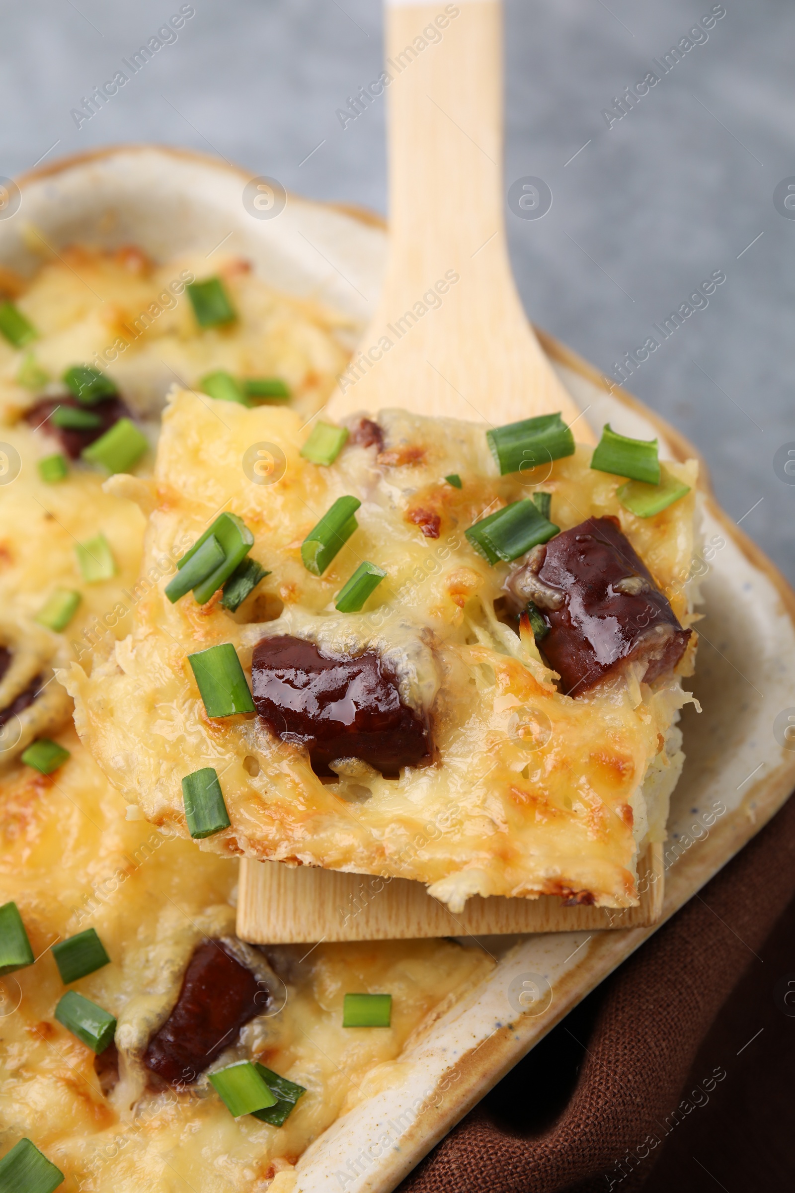 Photo of Taking piece of tasty sausage casserole from baking dish at table, closeup