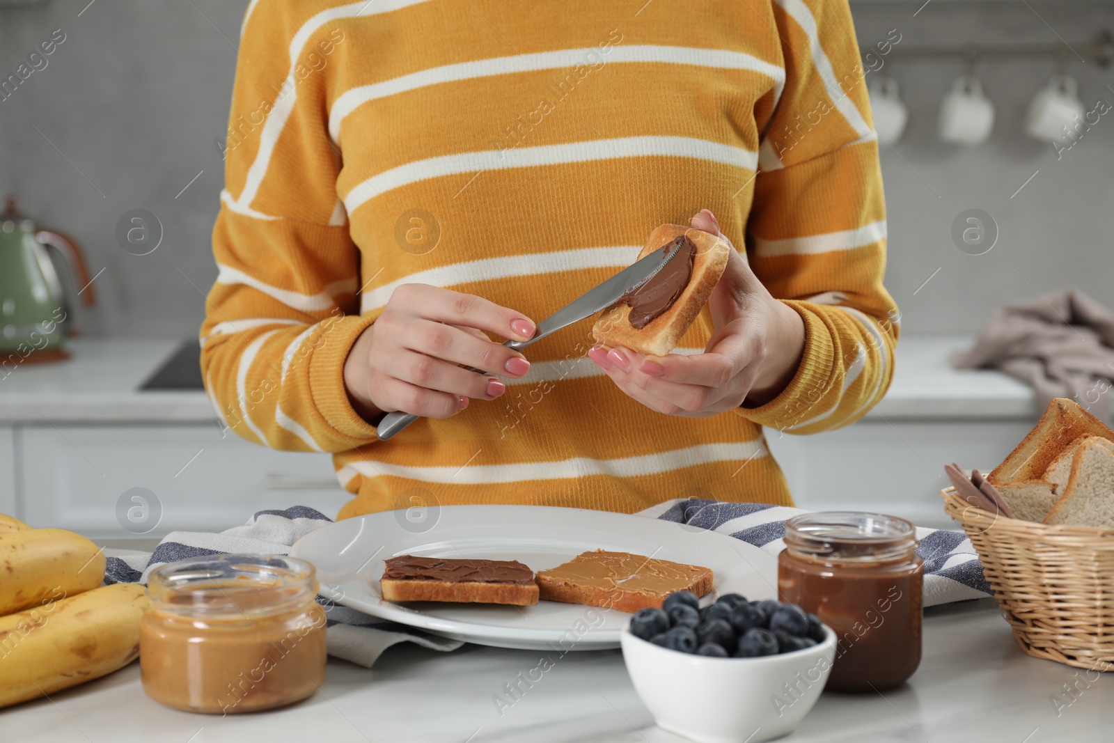 Photo of Woman spreading tasty nut butter onto toast at table, closeup